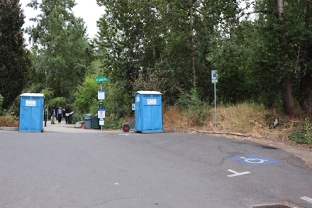 Accessible parking space &ndash; two porta potties &ndash; bike rack &ndash; park rules &ndash; dog bags and trash can at park entrance